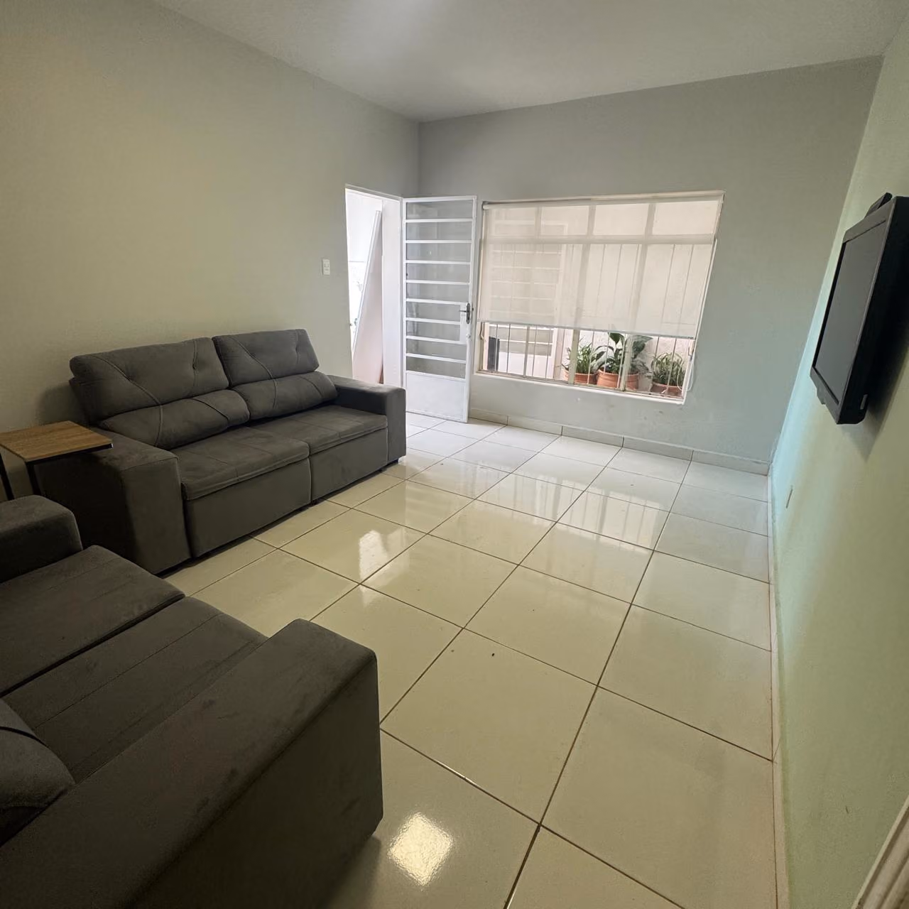 Cozinha compacta com bancada preta, pia de inox, fogão de mesa, armários cinza, geladeira branca, micro-ondas no nicho de prateleira de madeira e decoração com planta verde.